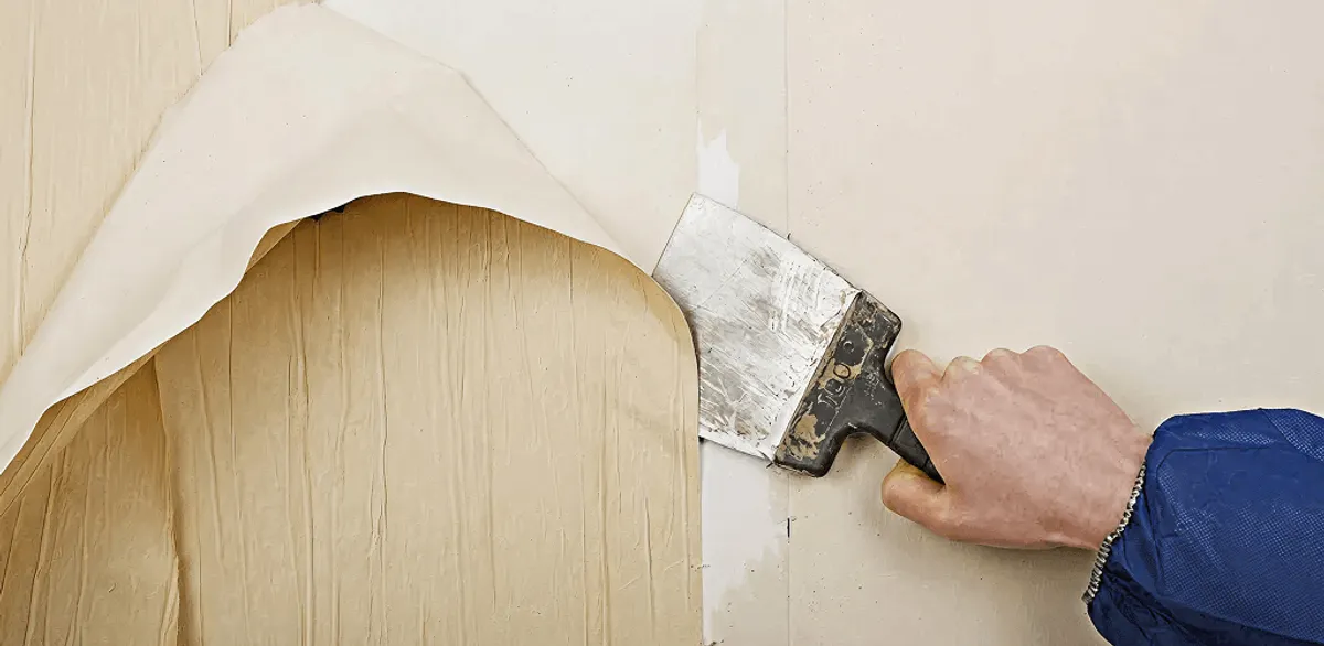 Handyman removing wallpaper with a scraper for wall preparation in Chandler, AZ