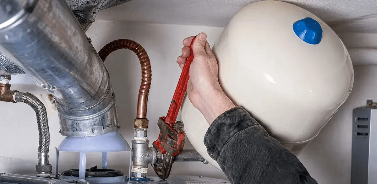 Water heater repair technician tightening plumbing connections near a tank unit in Chandler, AZ